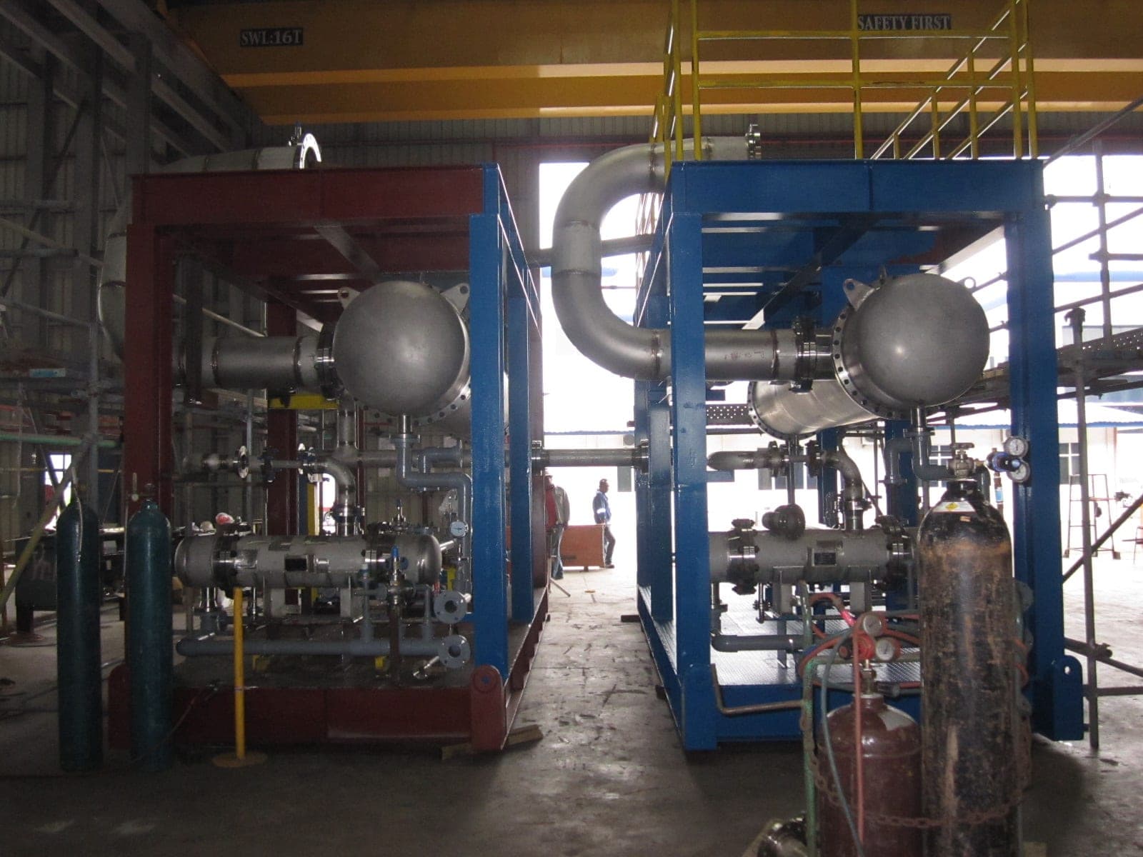 Workers assembling a fully piped process skid module inside a fabrication shop.